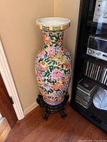 Full view of the colorful Chinese floor vase on its carved wooden stand placed on a wood floor.