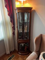 Curio cabinet in corner with glass shelves and wood frame, showing entire cabinet and surrounding area.