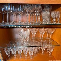 Top glass shelf showing clear long-stem wine glasses on the left, large crystal wine glasses with geometric cuts in the center, and smaller cut crystal tumblers with heavy etching on the right.