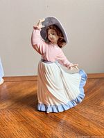 Front view of Nao by Lladro figurine showing girl holding hat and flowing skirt.