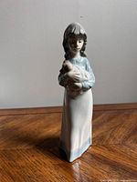 Front view of the glossy porcelain figurine showing a girl holding a small dog, emphasizing facial details and color.