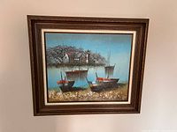 Framed nautical scene painting showing boats near shore, lighthouse, and houses under blue sky.
