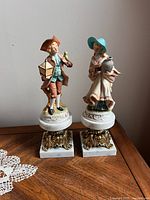 Front view of the pair of porcelain figurines standing side by side on marble and ornate gold bases.