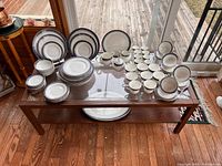 Full view of dinnerware laid out on a glass top table showing plates, bowls, cups, saucers and serving pieces