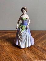 Front view of Royal Doulton Jessica figurine in period dress with green and purple accents standing on a wood floor.
