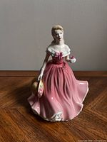 Front view of the Royal Doulton figurine depicting a young woman in a pink dress holding a hat and flower.