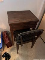 Front view of the closed wooden sewing table and upholstered chair