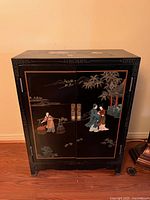 Front view of the small black lacquered Chinoiserie cabinet showing hand-painted scenes on doors and top with metal handles.