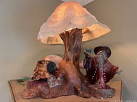 Front angle showing the mushroom lamp lit with the wizard and frog figurines on a tree root base.
