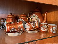 Full view of the vintage Hong Kong tea set including teapot, sugar bowl, creamer, cups and saucers displayed inside a glass cabinet.