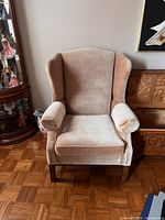 Front view of the vintage wingback chair showing overall structure, fabric condition, and wooden legs.