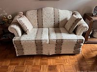 Front view of vintage upholstered love seat with two matching accent pillows, showing cream patterned fabric and rolled arms.