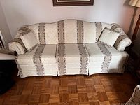 Full front view of the vintage upholstered sofa with three seat cushions and two matching pillows on hardwood floor.