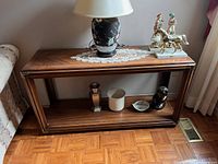 Front view of vintage wood console table showing top surface, brass accents on corners, and lower base with items placed on shelf for perspective only.