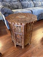 Front and side angles of wood hand carved side table with hexagonal shape and ornate floral and leaf carving.