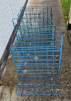 Three green-coated metal wire crab traps lined up on concrete outside near a wall and grass.
