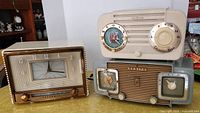Front view of three vintage radios with clocks on a surface including Sylvania, RCA Victor, and Zenith brands.