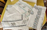 Three off-white vintage tablecloths stacked, showing embroidered camel and floral designs
