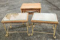 Three wicker tables on pavement: two with glass tops and cast iron legs, one larger wicker table without glass top