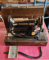 Front view of Singer Class 99 sewing machine on wooden base with carrying case, manual, and belt below.