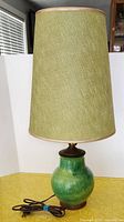 Full view of the lamp showing green ceramic base, tall green fabric shade, and brown cord.