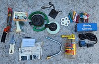 Photo of assorted garden tools and accessories laid on concrete including clippers, sprayer, bee water cups, and fountain pump with related parts
