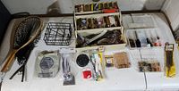 Wide view of fishing gear spread on table including net, wire basket, stainless steel wire pack, tackle boxes, flashers, grip tool, and miscellaneous packages.