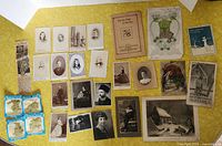 Full overview of old photographs, booklets, prints spread on yellow background showing various portraits, booklets, and smaller prints