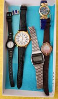 Five watches arranged in a box showing various strap types and dials including analog and digital