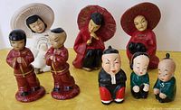 Front view of eight vintage Asian-themed figurines arranged on a yellow surface showing details of chalkware and ceramic finishes.