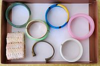 Lot of seven vintage bracelets in a cardboard tray seen from above, showing colors and designs.