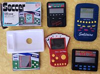 Six vintage handheld games including boxed Soccer LCD card game by Gakken, Electronic Classic, Solitaire Card Stacks, Bee 3-in-1 Poker, Pocket Poker, and one unbranded black game, laid out on yellow surface.