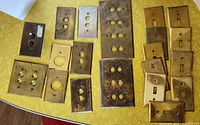 Various vintage light switch covers laid out on yellow table, showing different sizes, shapes, and switch configurations.