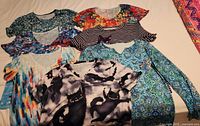 Eight women's t-shirts laid out featuring various colorful patterns including cats and floral designs in size medium or large.