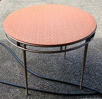 Full view of round table showing orange vinyl top and beige metal folding legs