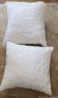 Two white cushions stacked, showing ruffled texture on front sides.