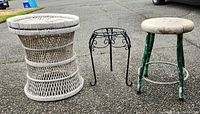 Photo showing all three items: white wicker plant stand, black metal plant stand, and vintage stool with green metal base and wood top.