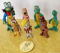 Front view of all six Pogo figurines and the pinback button arranged on a yellow surface