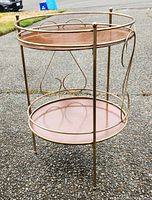 Front and angled view showing the gold-tone metal frame with decorative swirl details and two removable wood shelves.