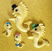 Four yellow ceramic fish wall plaques arranged on a yellow textured surface, showing the size differences and painted details of hats and accessories.