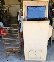 Photo of vertical electric smoker with open hinged lid showing blackened interior with metal rack beside it