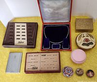 Overview photo showing ring trays, jewelry display box, cigarette case, and various trinket boxes on yellow surface.