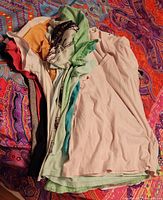 Stack of assorted women's t-shirts in solid and pastel colors, folded and stacked loosely on a colorful patterned fabric background.