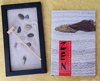 Zen sand garden with six stones and wooden rake next to Zen Rock Gardening book