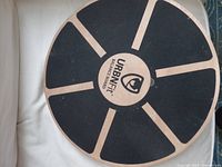 Top of round wooden balance board showing black non-slip surface with URBANfit logo in center.