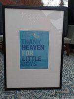 Full view of framed nursery print showing black frame, white matting, and blue print with text and bird.