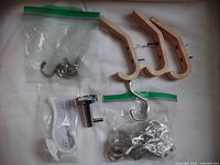 Three wooden wall hooks, screws visible, placed on a white surface with two plastic bags containing metal hooks and one metal hook with packaging.