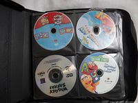 Photo of four DVDs inside transparent plastic sleeves in a black binder. Visible DVDs include The Wiggles and Sesame Street titles.