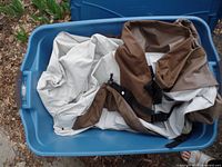 Blue plastic bin with five patio furniture covers including four chair covers and one loveseat cover in beige and brown colors.