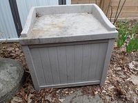 Closed view of small rectangular light gray plastic deck box with slight dirt and wear from outdoor use.